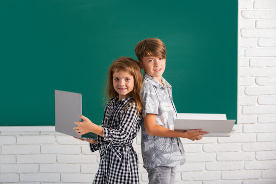 Portrait of children boy and girl with laptop computer and book at school. Kids in class on blackboard.