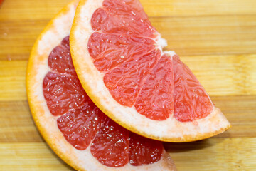 sliced pink grapefruit on a wooden board. home environment.half of a slice.healthy food,diet,slim,fit. lose weight. fibers.vitamin c from fruits red color juicy sour acrid taste
