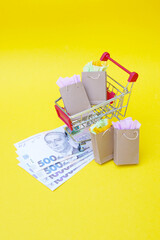 Shopping cart with paper bags and Ukrainian hryvnia on a yellow background.