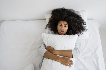 Scared mixed race woman lying on bed, hug pillow