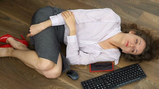 Tired young female office manager is lying on the floor with keyboard, mouse and smartphone, lay flat movement, routine work, freelance, burnout syndrome