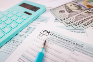  1040 tax forms with calculator, dollars and pen.