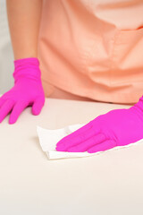 Close up of hands in rubber protective pink gloves cleaning the white surface with a white rag