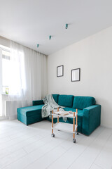 Minimalistic interior design studio apartment with white walls and a turquoise green sofa. Living room and dining room for a comfortable life
