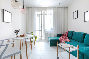 Minimalistic interior design studio apartment with white walls and a turquoise green sofa. Living room and dining room for a comfortable life
