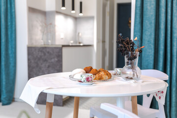 Minimalistic design of a white studio apartment. Round dining table with breakfast, cozy room for living