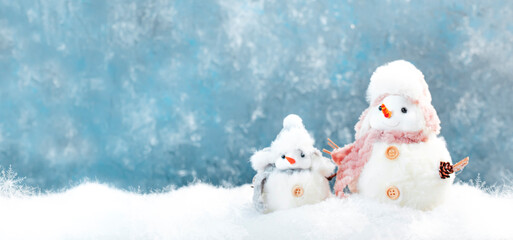 Christmas and new year snow concept with two cute snowmen in hats and scarves in snowdrift on blue background