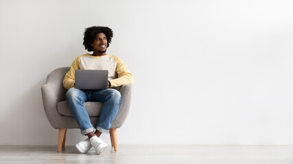 Smiling Black Guy With Laptop Computer Sitting In Chair And Looking Aside