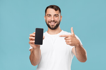 Friendly glad mature caucasian male show finger to smartphone with empty screen to camera