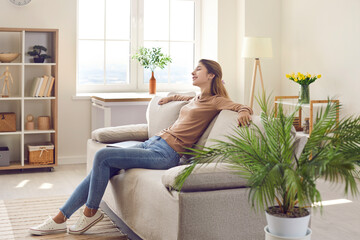 Happy relaxed woman resting on comfy couch in modern interior of her own apartment. Young girl...