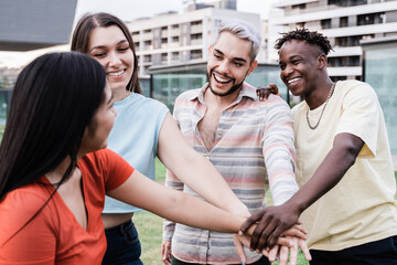 Young diverse group of people celebrating together stacking hands outdoor - Focus on gay man wearing makeup - obrazy, fototapety, plakaty