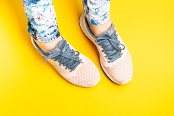 Woman’s legs in pink sport sneakers on bright yellow background top view. Healthy lifestyle and fitness concept. Bright sport store and fitness gym banner.