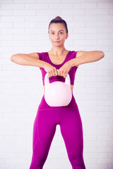 Fototapeta na wymiar retrato de profesora de yoga y pilates sonriente en un gimnasio con una pesa impartiendo lecciones con ropa violeta en un fondo de pared de ladrillo blanca