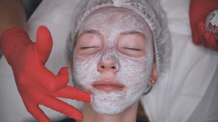 Application of a cream mask on the face of a girl with problem skin in the salon.