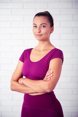 Fototapeta na wymiar retrato de profesora de yoga y pilates mujer joven sonriente en un gimnasio con una pesa impartiendo lecciones con ropa violeta en un fondo de pared de ladrillo blanca