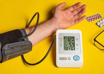 Person measures their own blood pressure at the yellow medical table. Taking care of your own health. Digital blood pressure machine shows a good result