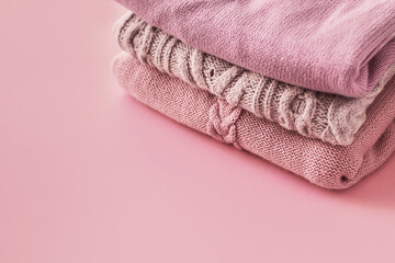 Fototapeta na wymiar Stack of cozy winter autumn sweaters in pink pastel colors on a pink background. Knitted wool sweaters. Fashion and style. Copy space.
