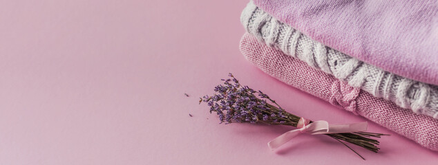Background with warm sweaters. A pile of knitted clothes and a bouquet of lavender on a pink background. Knitwear, place for text, autumn-winter concept. Copy space Selective focus. Banner