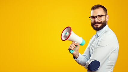 Horizontal fofo of handsome caucasian male holding megaphone while smiling, isolated over yellow backdrop, empty space
