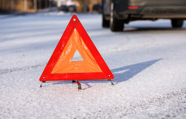 The red triangle of an emergency stop on a winter road at the place of a car stop. There is a silhouette of a car in the background.