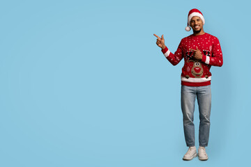 Cheerful handsome black guy in Santa hat showing copy space