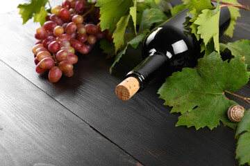 Close up of red wine bottle with stopper and grapes and green grapes leaves on dark wooden table...
