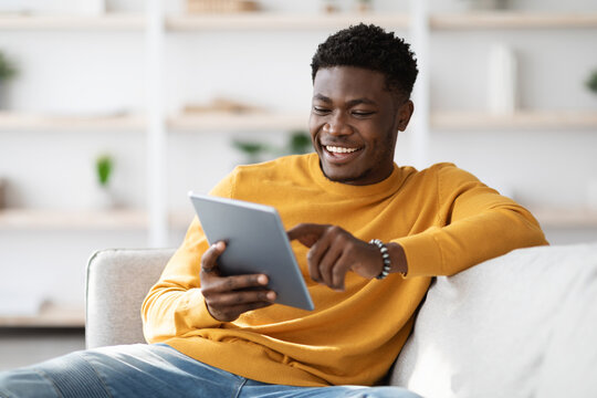 Smiling african american man sitting on couch with digital tablet