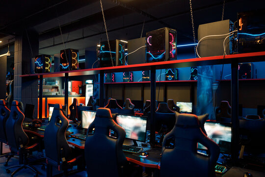 Photo of powerful computers for esports online competitions and streaming chairs in interior of dark, empty internet cafe