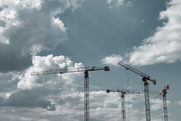 Construction cranes work on creation site against sky background