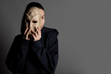 Hiding behind a mask, a young woman in a dark hoodie hides her face with a mask, the concept of...