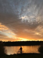 Silhouette of a man with a bicycle on the background of the lake and sunset.