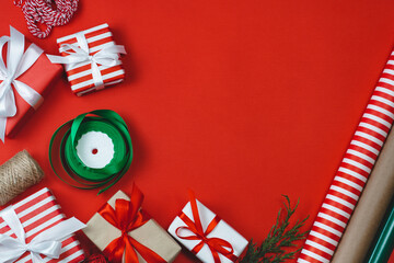 Flat lay of decorated gift boxes, wrapping paper rolls and ribbons on red background