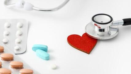 Blue pills with blister packs and stethoscope head on red heart on white background.