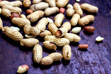 Unpeeled brown peanuts on textured black metal background.
