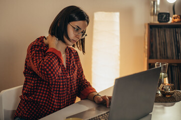 Beautiful woman having back and neck pain while using laptop at home