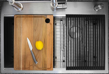 Workstation kitchen sink. A lemon and a knife placed on a cutting board just above the double bowls.