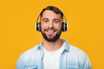 Cheerful adult attractive european man in headphones listening to favorite music