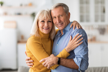 Loving Senior Couple Embracing Smiling To Camera At Home