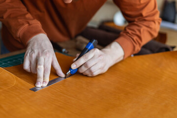 Male tanner making cutting scheme of bag working at leather workshop. Handcrafted creating
