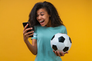 Photo of soccer fan girl holding ball in hand and looking at mobile phone screen with amazed face...