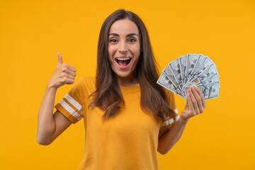 Happy girl holding a ward of dollar banknotes and showing thumbs up