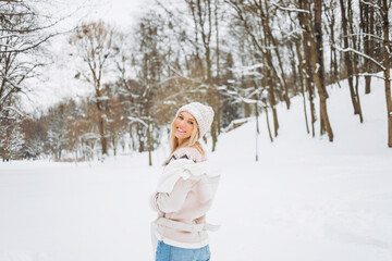 Fototapeta na wymiar Close up portrait of an beautiful girl in a woolen sweater enjoying winter moments. Outdoors photo of a short-haired lady in a pink hat having fun on a snowy morning on a blurred nature background.