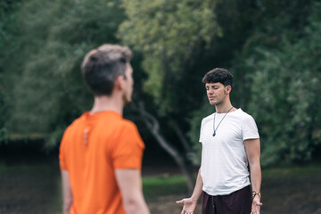 Naklejka premium Men standing facing each other while doing yoga outdoors