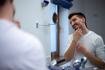 A guy with a patchy beard looks in the mirror