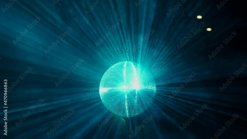 Poster a mirrored disco ball is spinning at a party. blue rays of light are reflected from it in the smoke.