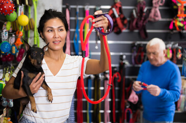 Positive asian woman choosing and buying leash for her doberman pinscher dog at a pet shop