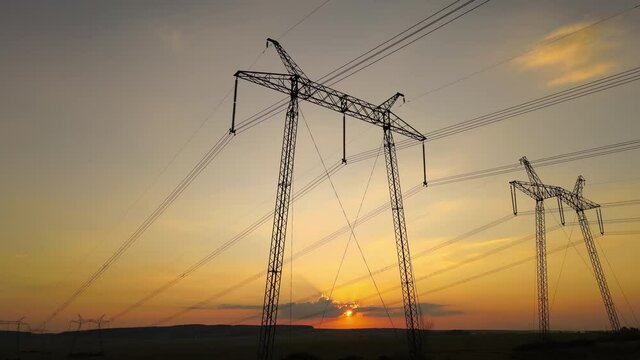 Dark silhouette of high voltage towers with electric power lines at sunrise