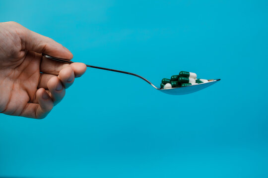 Human hand holding a tablespoon with colored pills. Closeup. Space for text. Pharmacology and medicine struggle for health. Medicine and health concept
