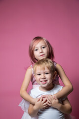 Caucasian brother and sister ,hugging on camera on pink background studio shot.