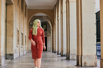 Alternative woman with green hair and red dress walks in old building